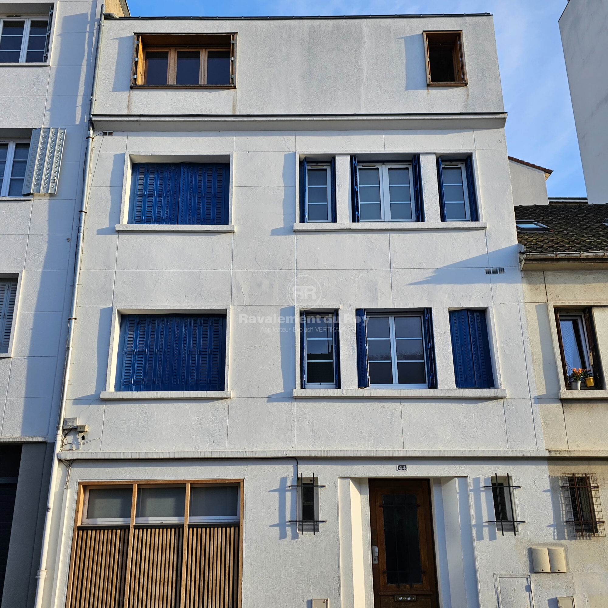 Façade blanche de bâtiment avec fenêtres à volets bleus et porte en bois