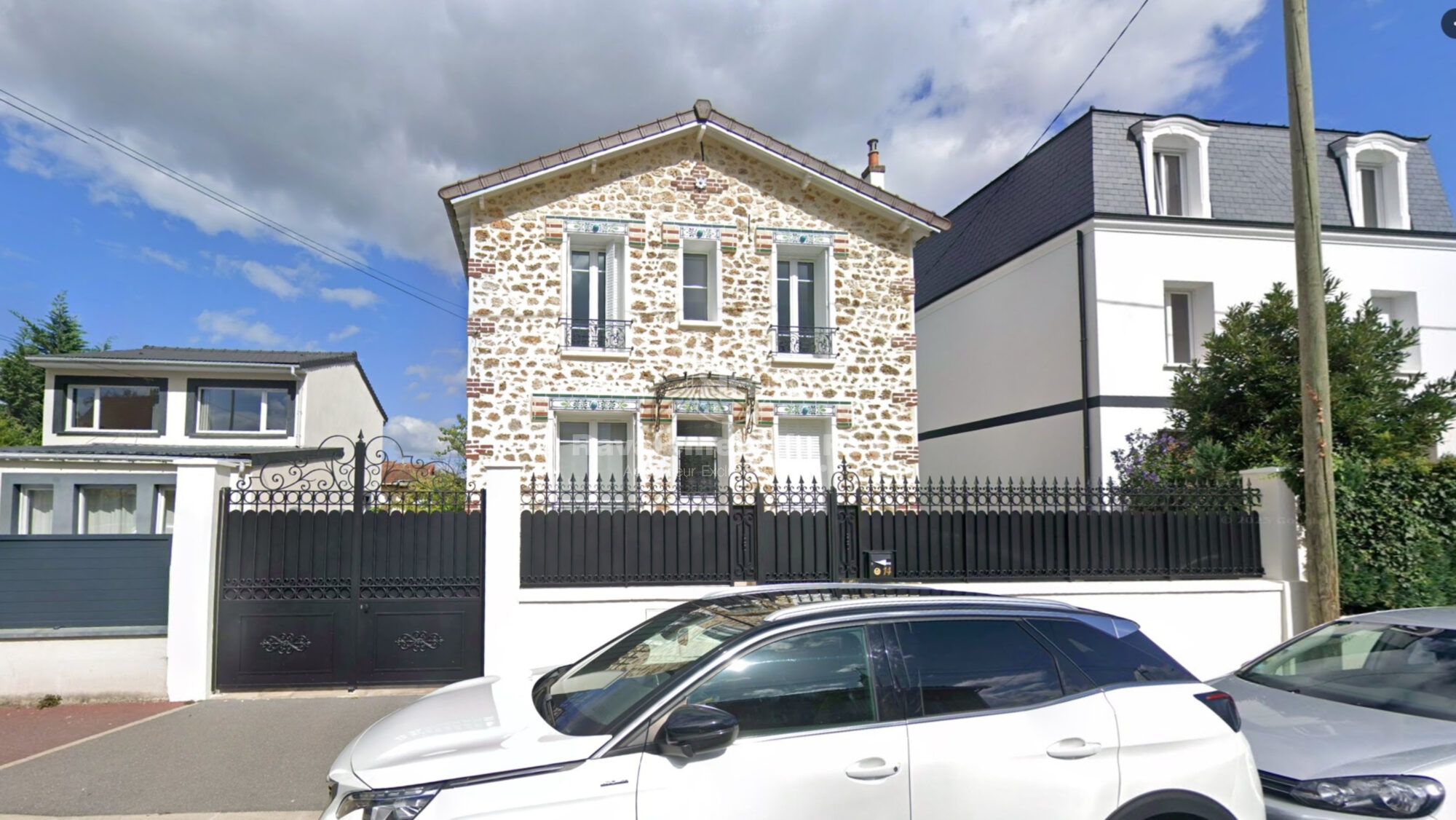 Maison en pierre avec clôture en fer noir et voiture blanche garée devant