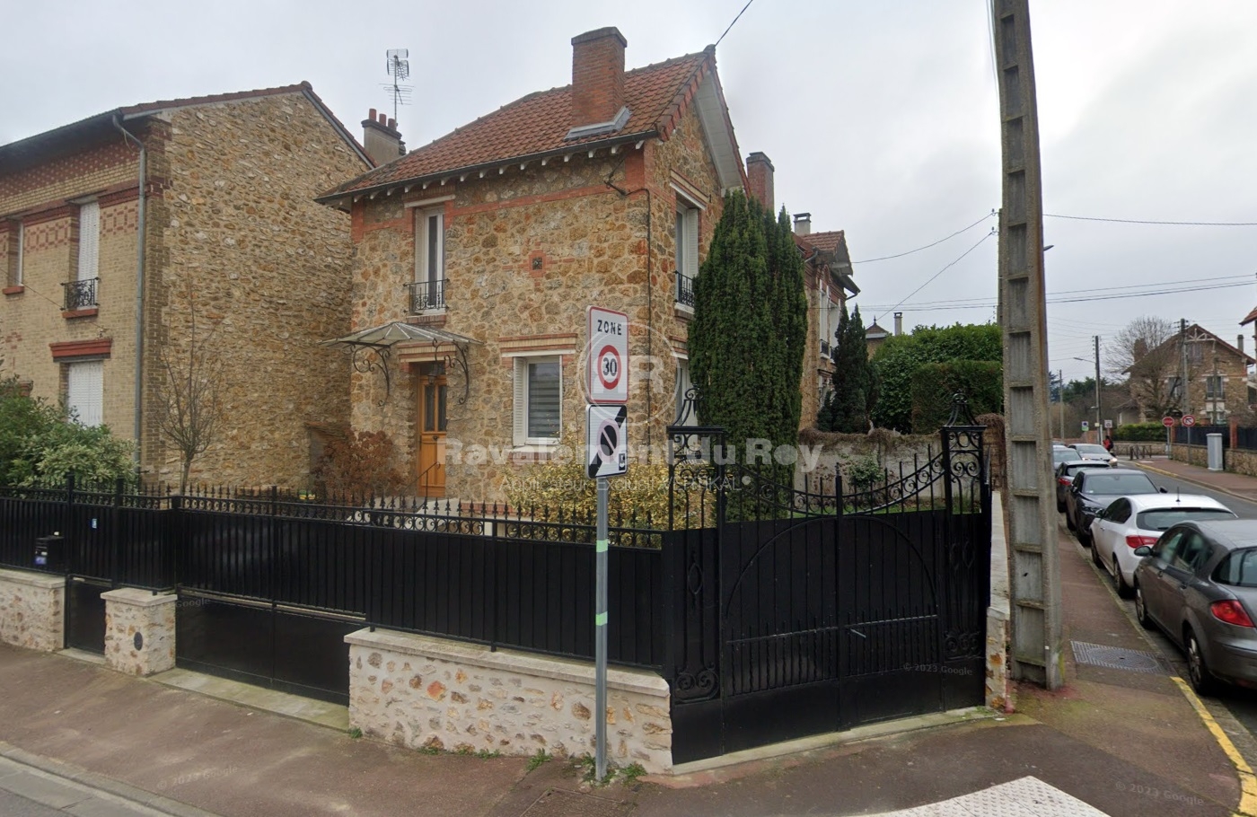 Maison en pierre avec grille noire et signalisation routière