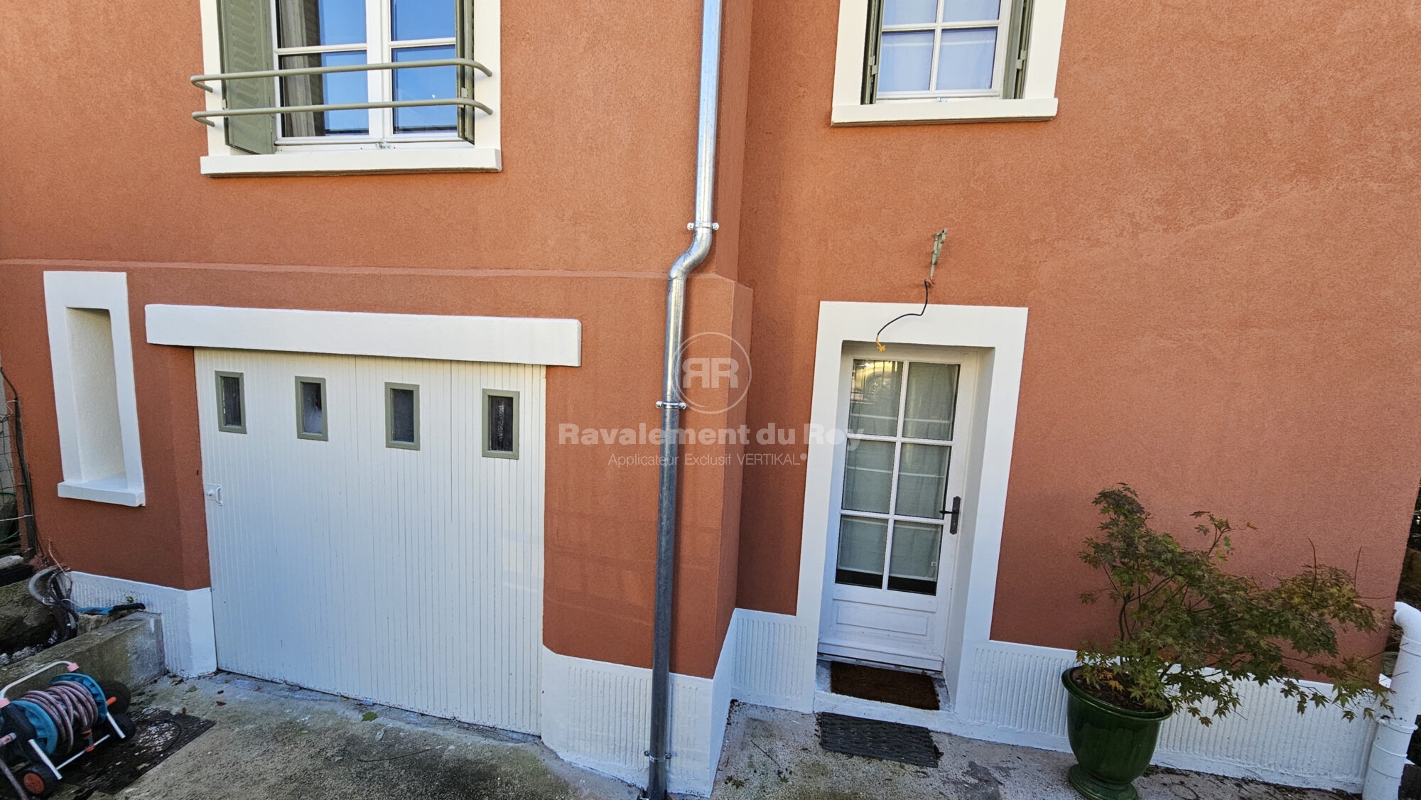Façade en ravalement avec porte blanche et garage sur une maison orange