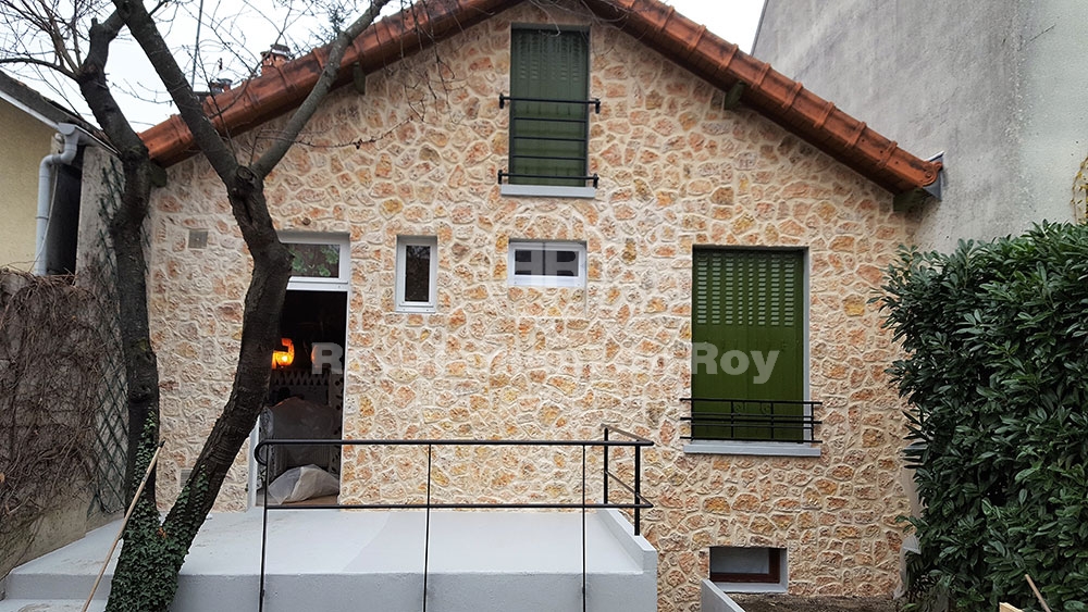 Maison en pierre avec fenêtres vertes et balcon